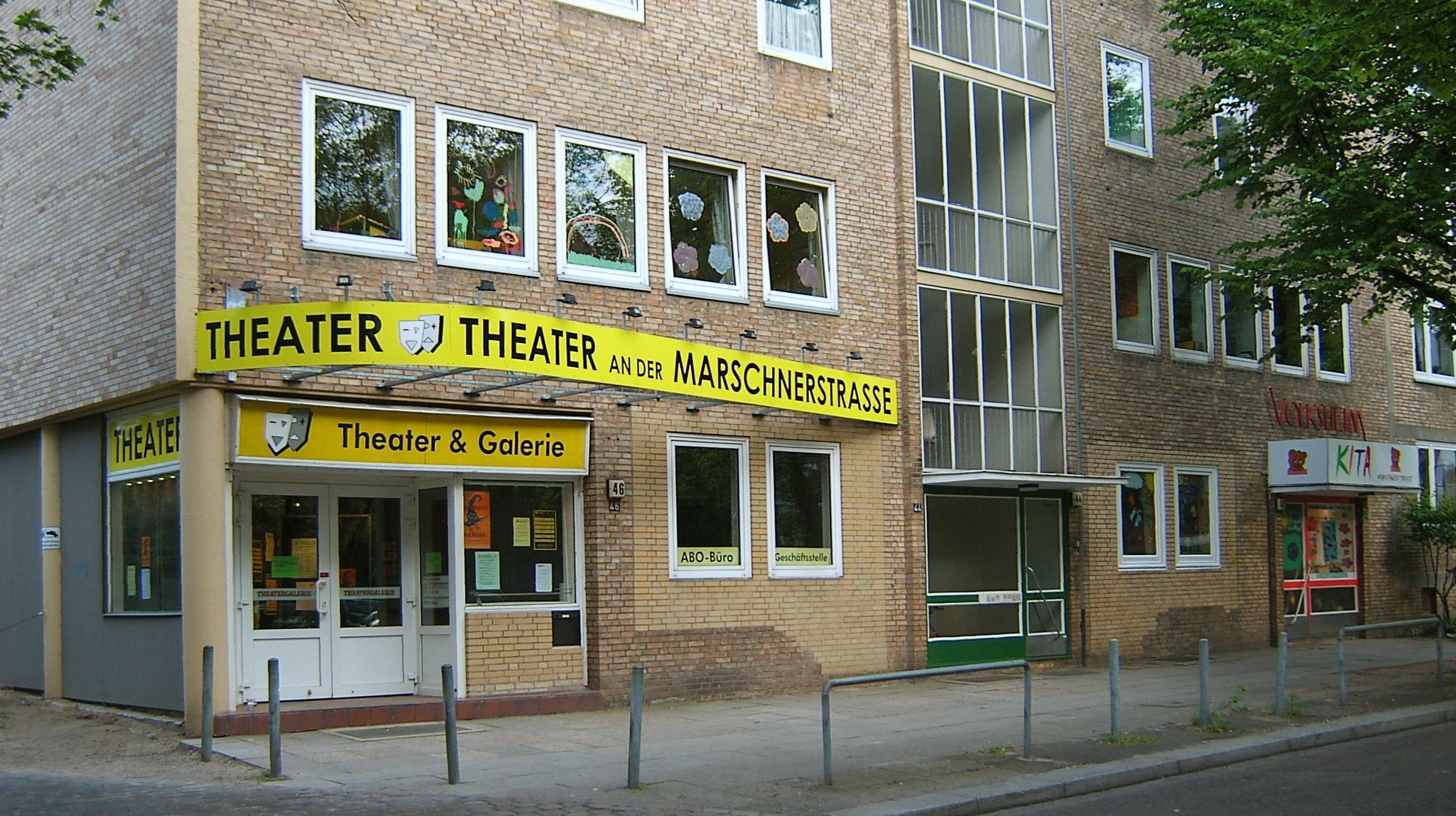 Fassade des Theaters an der Marschnerstrasse: gelbes Banner „Theater an der Marschnerstrasse“, Eingang mit Schild „Theater & Galerie“, ABO-Büro und Geschäftsstelle